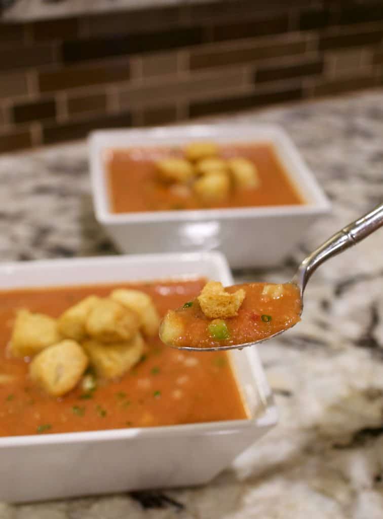 A spoonful of gazpacho in front of two white bowls of gazpacho