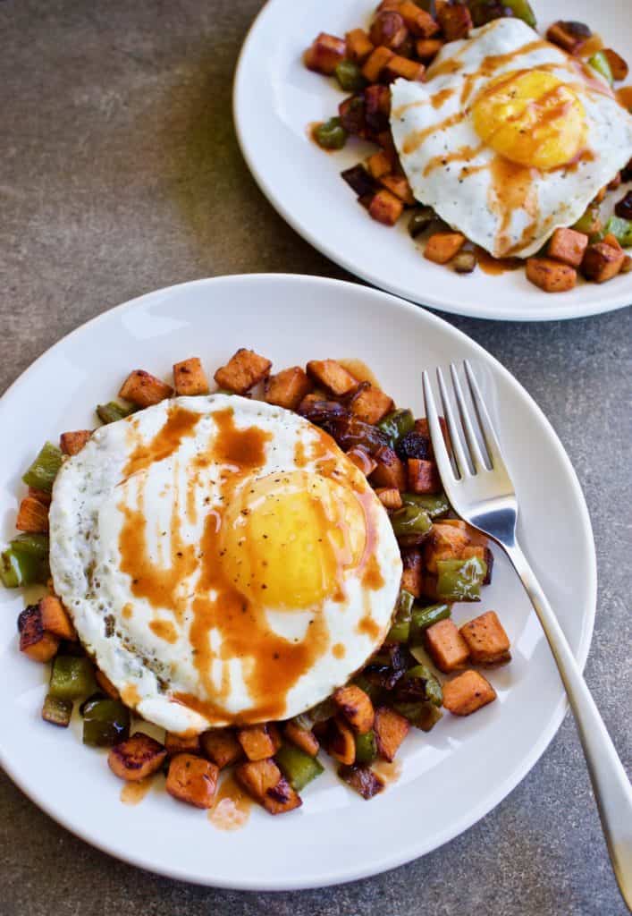 Overhead view of two plates of chipotle sweet potato hash with a fried egg and a fork