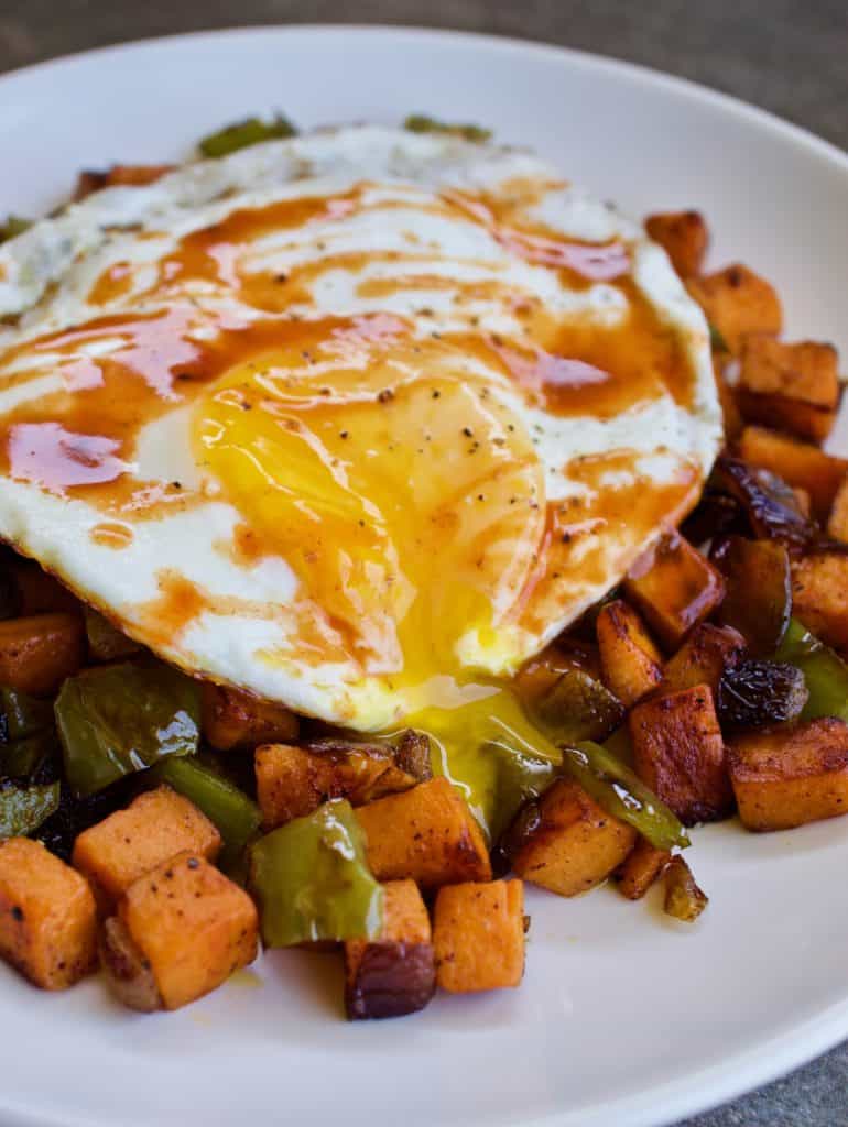 Close up angled view of chipotle sweet potato hash with a fried egg with a broken runny yolk