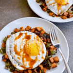 Overhead view of 2 plates of chipotle sweet potato hash with fried eggs and a fork, with banner text at top