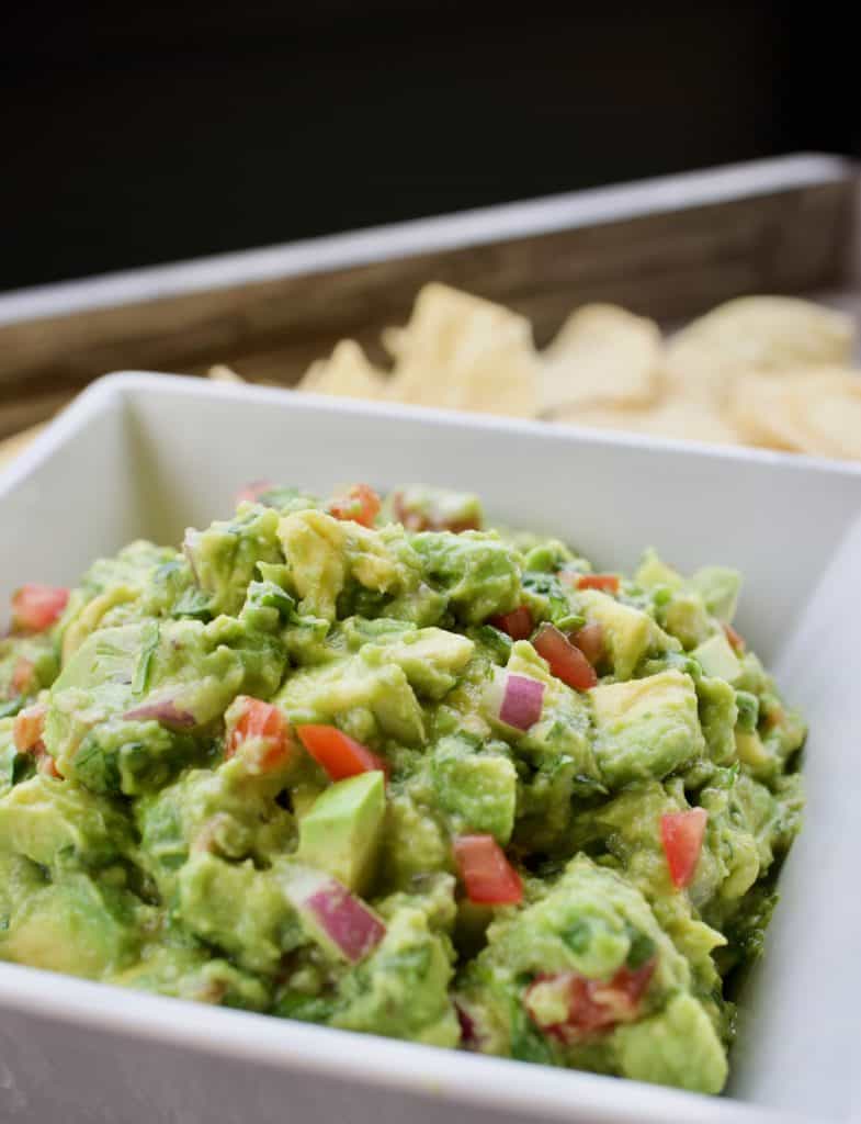 Guacamole in a white bowl surrounded by tortilla chips