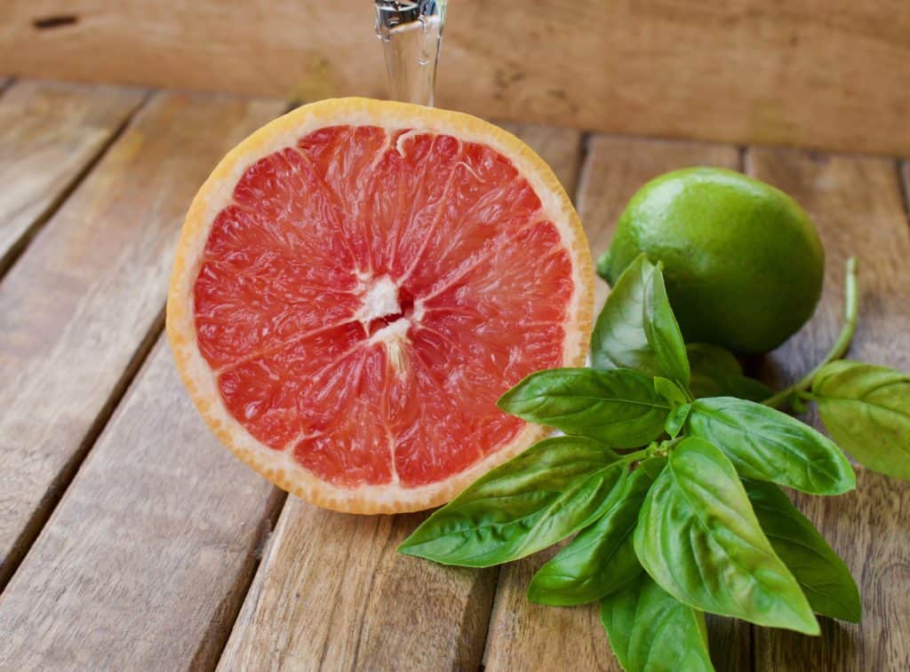 Closeup image of a sliced grapefruit, some basil, and a lime