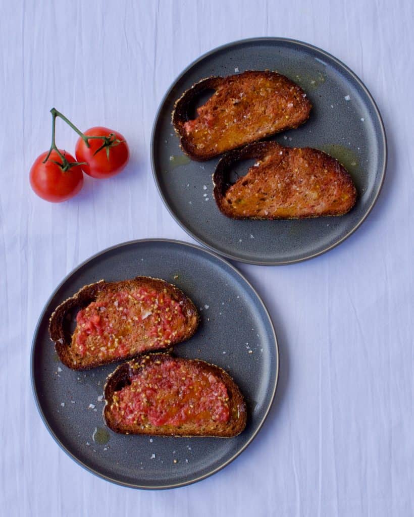 Four slices of pan con tomate on two grey plates