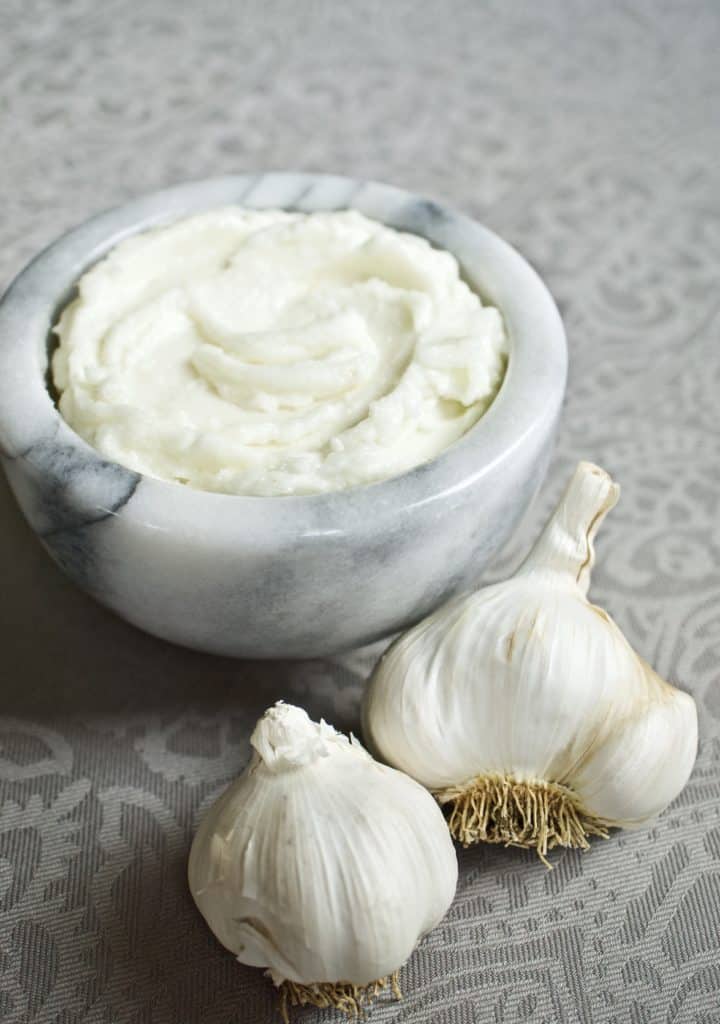 Lebanese garlic sauce (toum) in a small bowl surrounded by garlic