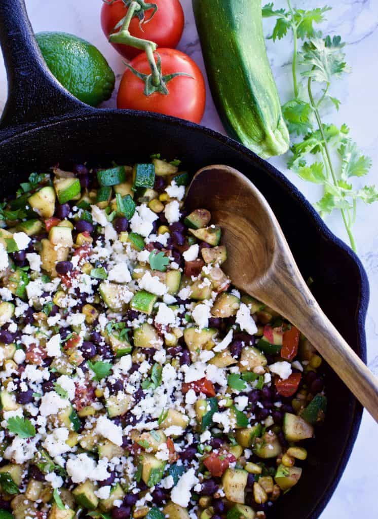Mexican veggie skillet in a cast iron pan with a wooden spoon