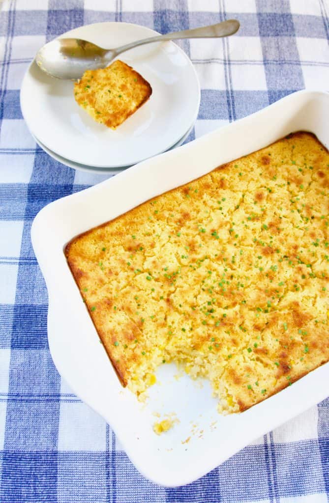 A serving of Southern corn pudding on a plate next to a serving dish