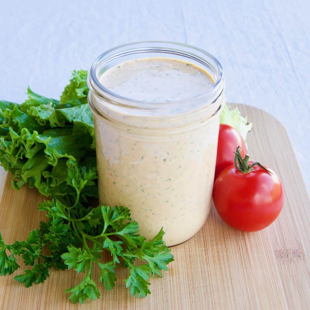 Magical chipotle ranch dressing in a mason jar surrounded by greens and fresh tomatoes