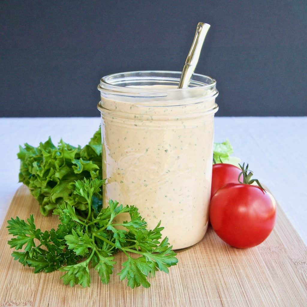 Magical chipotle ranch dressing in a mason jar surrounded by greens and fresh tomatoes