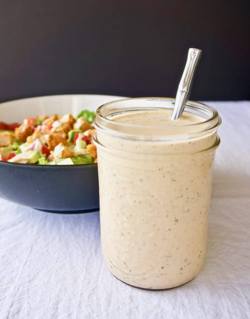 Magical chipotle ranch dressing in a mason jar in front of a bowl of salad