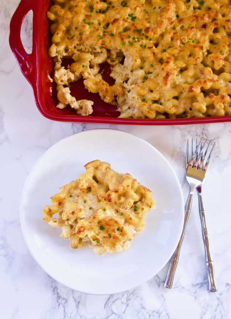 Spicy mac and cheese on a small plate next to a red baking dish