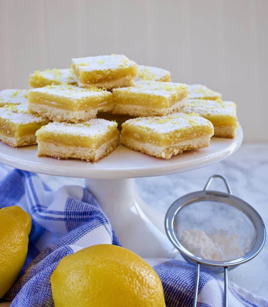 Classic lemon bars stacked on a white serving pedestal