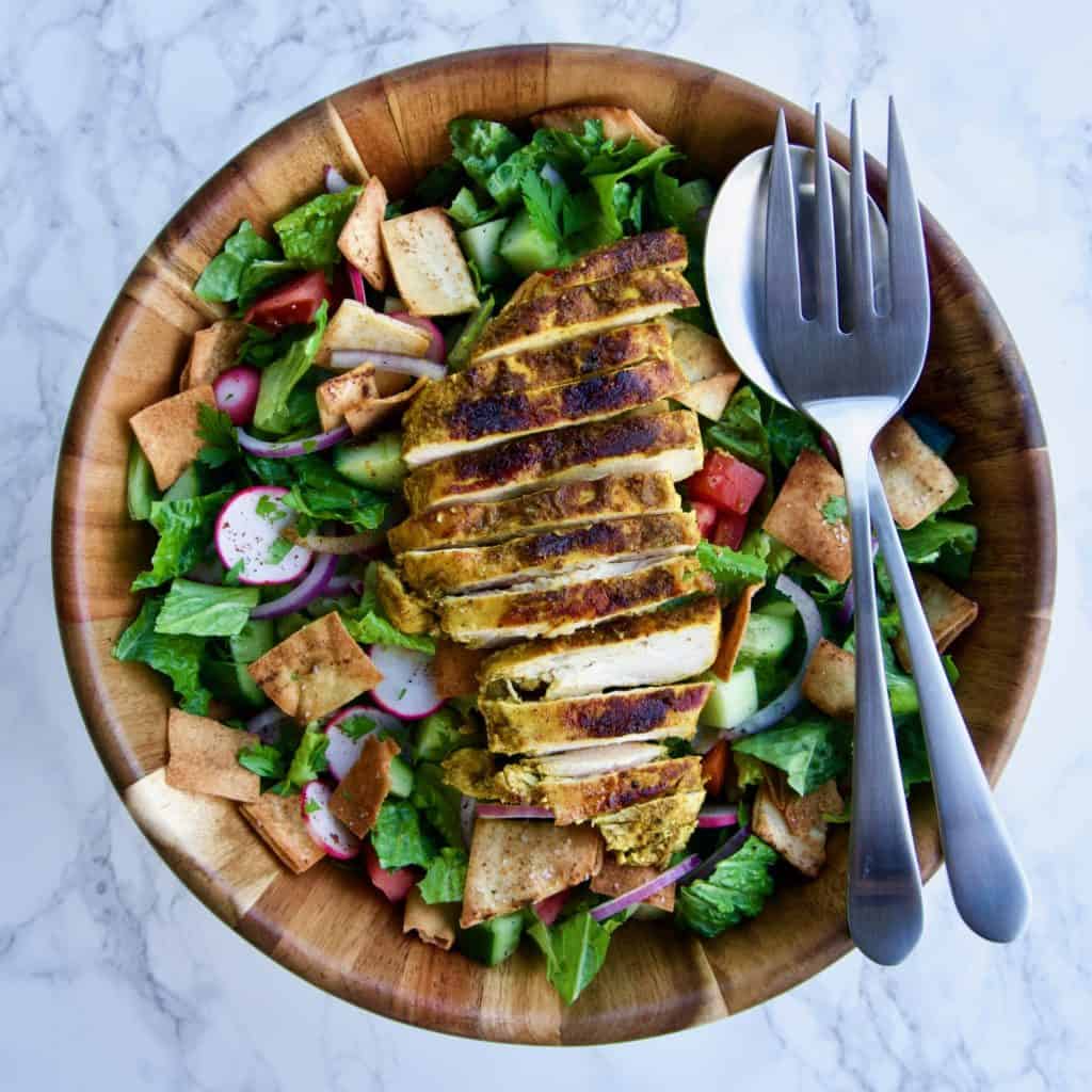 Fattoush salad with shawarma-spiced chicken in a wooden bowl with serving utensils
