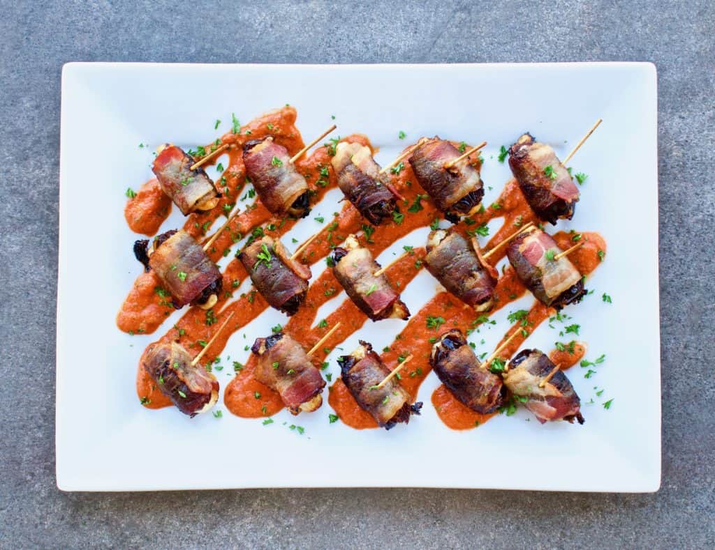 Bacon wrapped dates with romesco sauce on a white serving platter