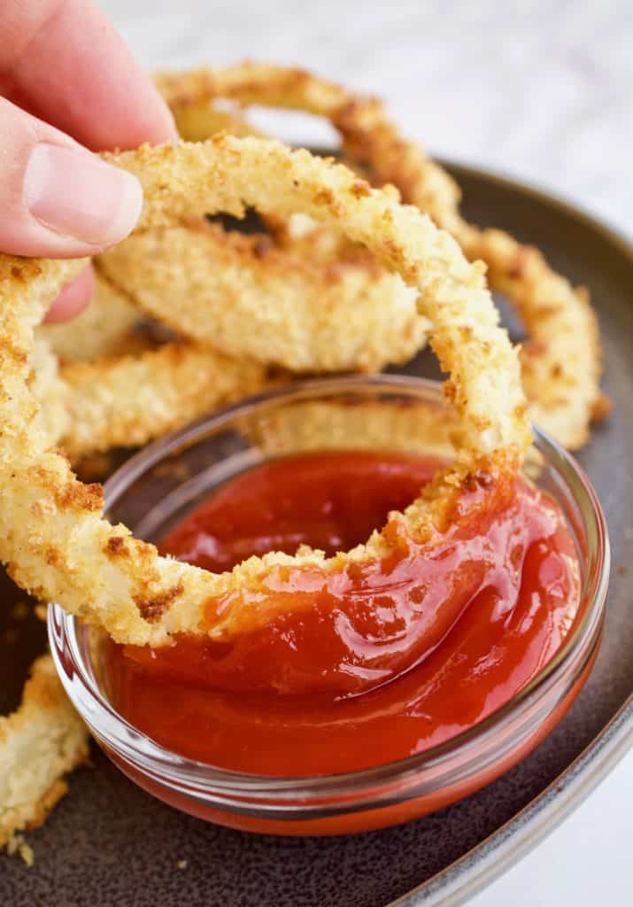 Close up of panko breaded baked onion ring dipping into ketchup