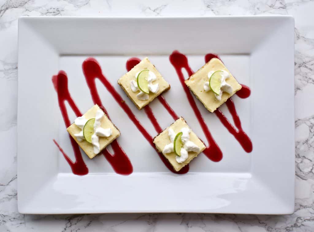 yummy noises key lime cheesecake bars with raspberry sauce on rectangular plate