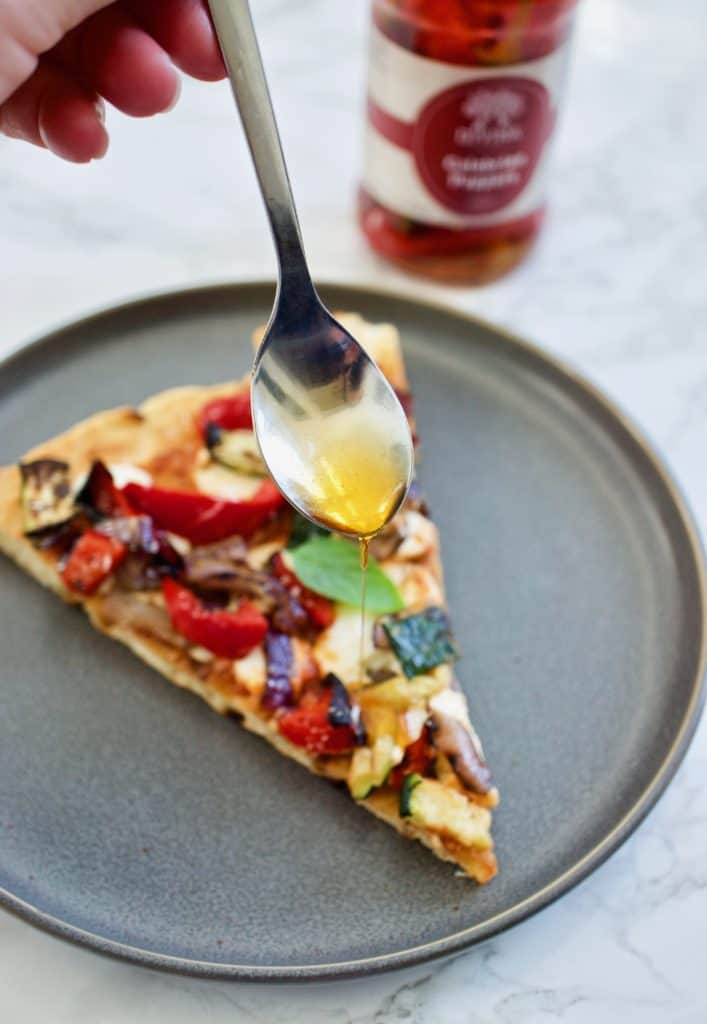 Spoon drizzling Calabrian Chili oil onto pizza slice
