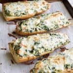 Four spinach artichoke french bread pizzas on parchment paper