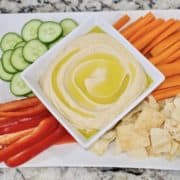 Authentic creamy hummus in a bowl surrounded by veggies and pita chips