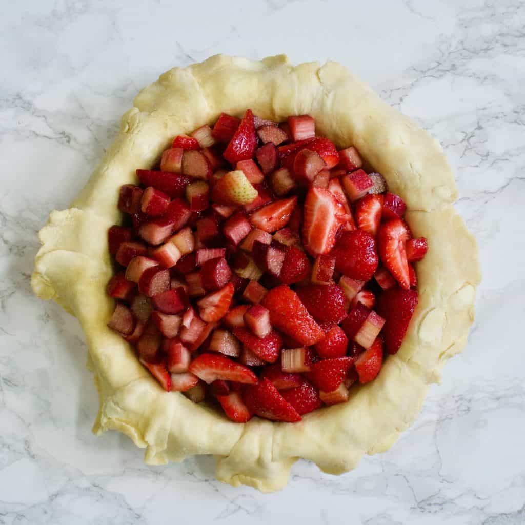 strawberries and rhubarb in pie plate with dough overhanging edges