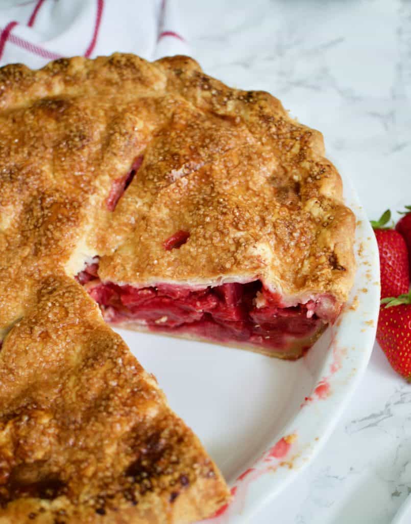 Strawberry Rhubarb Pie in a white pie plate with with a slice missing