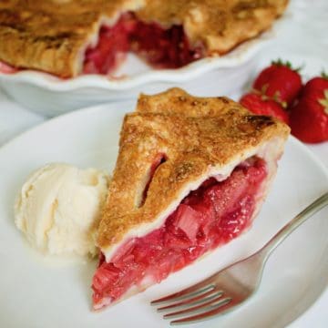 Slice of Strawberry Rhubarb Pie on a white plate with scoop of vanilla ice cream and fork