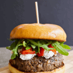 Blended mushroom and beef burger with goat cheese, roasted red peppers and arugula on a brioche bun on a small wooden board with header text