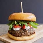Blended mushroom and beef burger with goat cheese, roasted red peppers and arugula on a brioche bun on a small wooden board