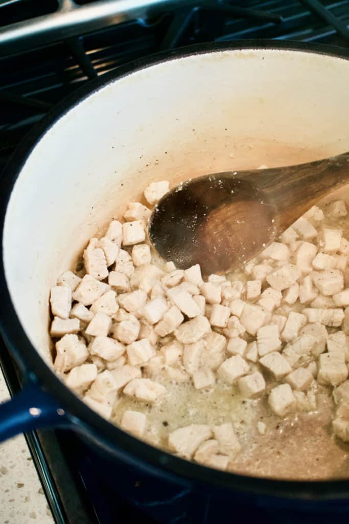 diced chicken cooking in a pot with a wooden spoon