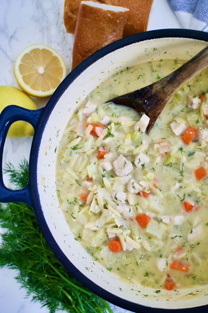 Lemon Chicken Orzo Soup in pot with wooden spoon next to dill, lemon and bread